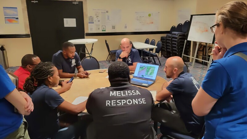 Response team members huddle around a laptop displaying a damage map of Jamaica.